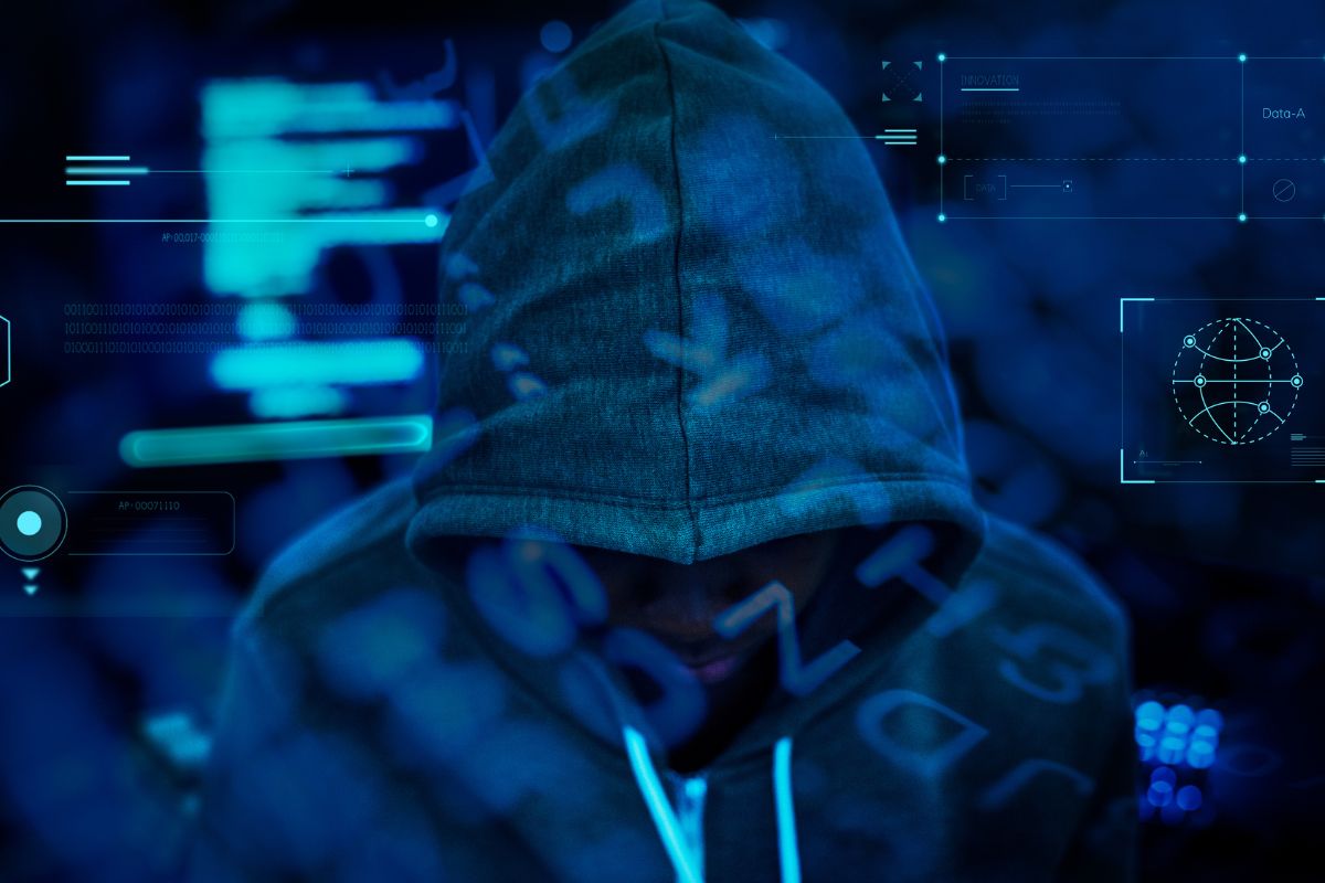 In this image, a person wearing a hoodie is standing in front of a digital background with various cybersecurity icons and symbols. The person is looking down at their phone, which is displaying a message or notification. The image is intended to represent the increasing threat of cybersecurity threats or attacks on businesses in Qatar in 2023.